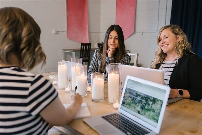 3 women sitting around a table with laptops