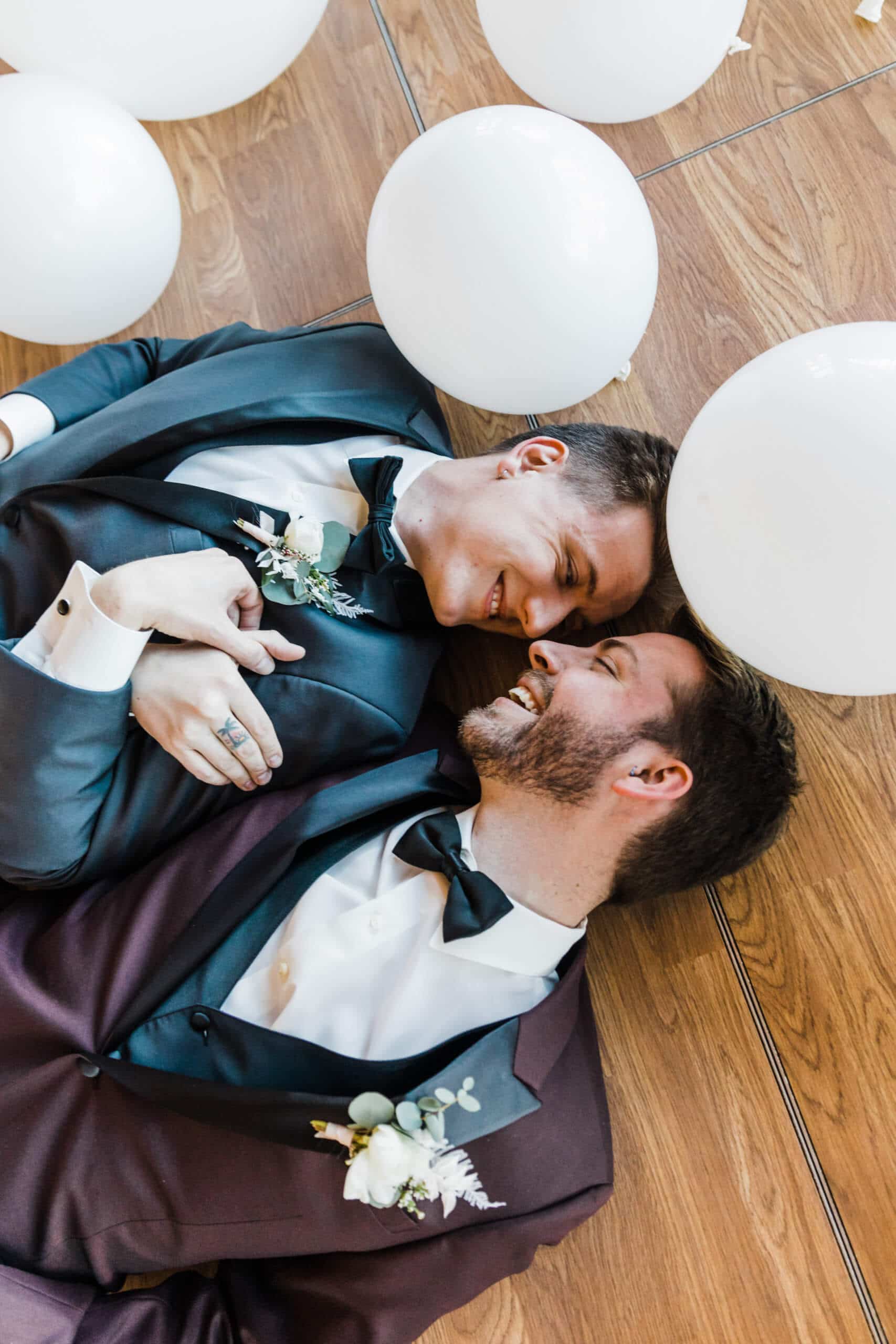 two men in suits laying on floor holding hands