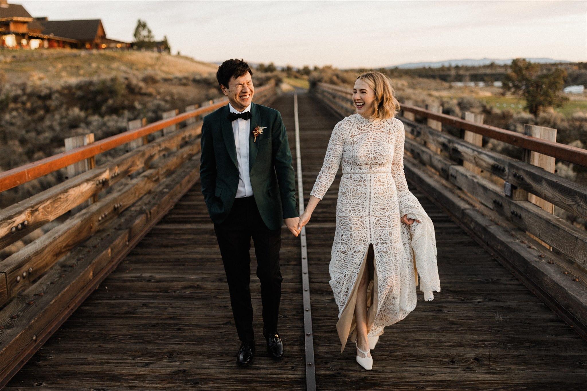 couple holding hands walking on a bridge, bride in white wedding dress. Groom in a suite